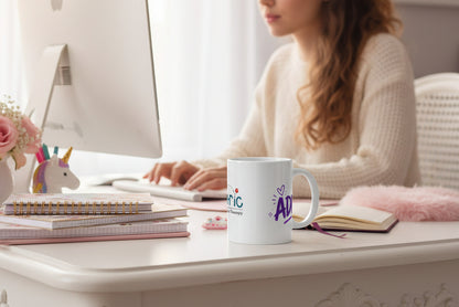 White mug with colorful text and graphics on a girls desk with her working in the background