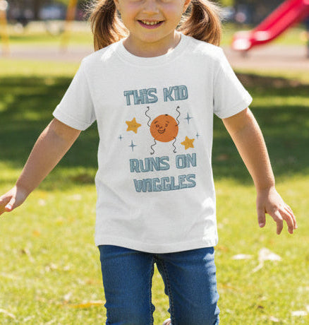 White t-shirt with a colorful graphic and text on a young girl with pigtails running in a park