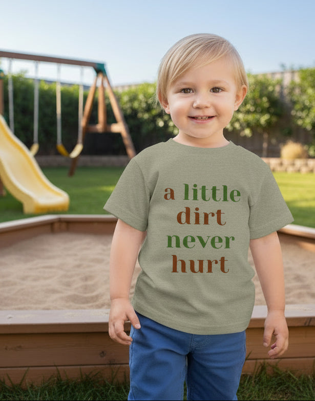 Child wearing a green t-shirt with 'a little dirt never hurt' text on sandbox outdoor background