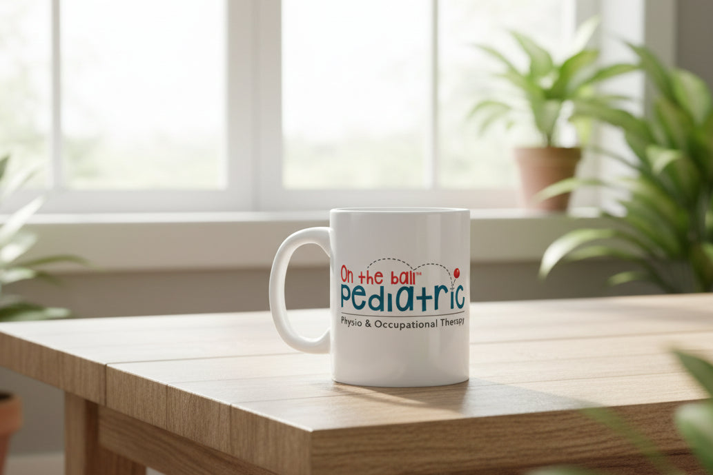 White mug with 'On the Ball Pediatric Physio & Occupational Therapy' text on a home background with plants and a window